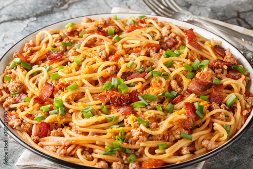Delicious spaghetti with bacon, minced meat, cheddar cheese, onion and spicy tomato sauce close-up in a plate on the table. Horizontal