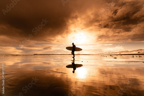 Woman standing on beach with surf board winter iceland sunset photo