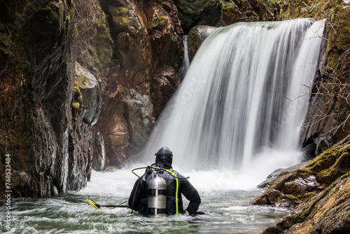 Rear view of scuba diver standing in river looking at waterfall photo