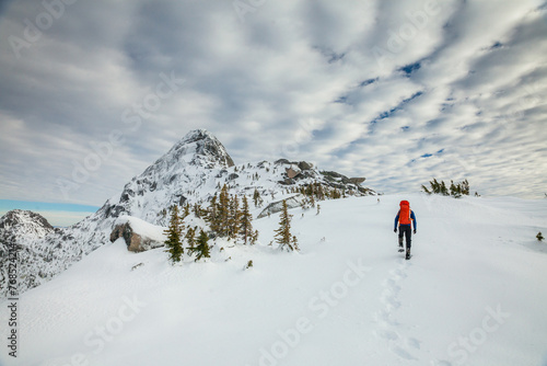 Hiker approaches mountain summit wearing snowshoes, leaving footprints photo