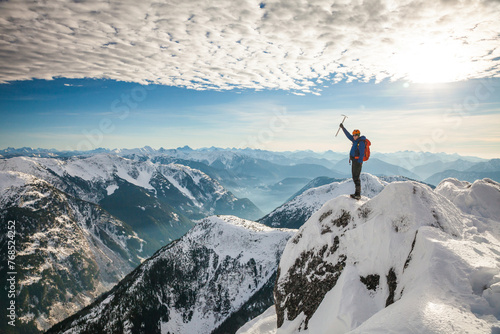 Mountaineer raises his ice axe on the summit of a mountain photo