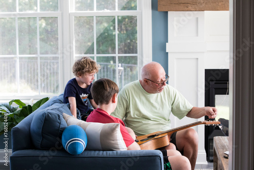 Grandpa Fixes Guitar Strings While Teen and Preschool Grandsons Watch photo