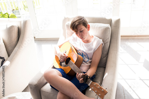 Teen Boy Sits in Sunshine Learns To Play Guitar photo