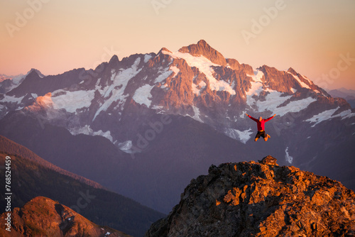 A hiker jumps off rocky cliff  in North Cascades National Park. photo