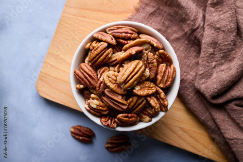 Top view, close-up of raw pecans in a bowl on the cutting board on gray background.