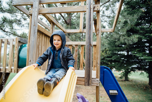 Smiling toddler sitting on slide on swingset in yard at home. photo