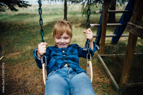 Small boys smiles while swinging on swing set in rural countryside. photo