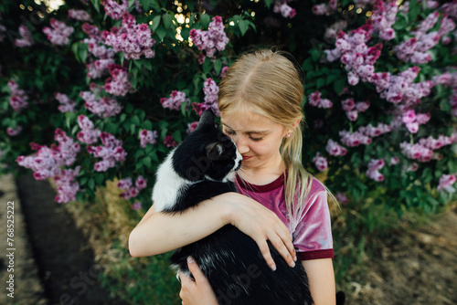 Preteen girl cuddles with cat in front of lilac bush in summer. photo