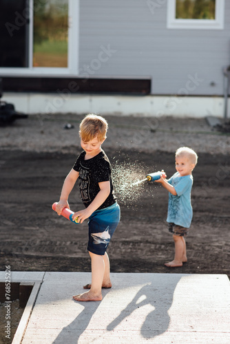 Young boy shoots another boy in the back with a water gun outside. photo