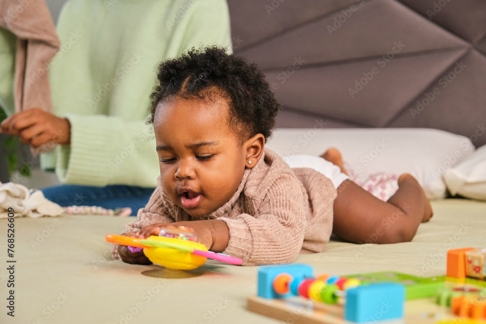 Cuban toddler playing while her mother change her clothes on bed. Cuban toddler playing while her mother change her clothes on bed.