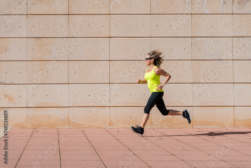 adult woman running along white pattern wall while doing workout photo