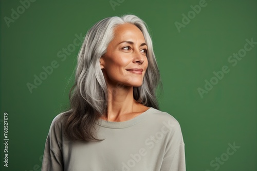 Thoughtful mature woman with grey hair looking up over green background