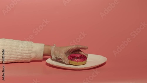 Close up of a hand putting pink donut on the white plate over the pink background. Cookery. Desert.