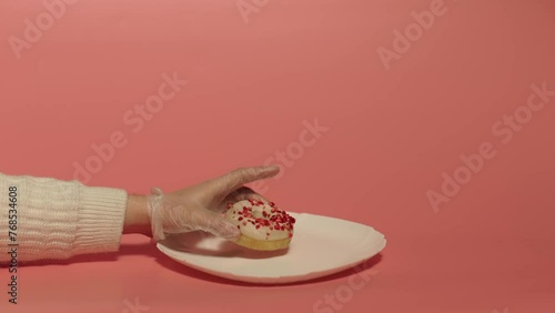 Close up of a hand putting white donut on the white plate over the pink background. Cookery. Desert. Food.