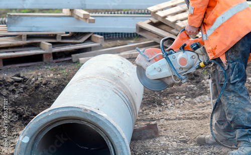 Construction worker cutting concrete pipe for drainage using a cut-off saw. Cutting concrete with a diamond blade creating cloud of silica dust