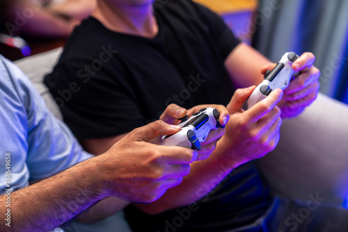 Close up of photo in holding joystick  playing video game or online streamer with friends in neon blue light curtain background. Concept of sitting couch lifestyles gamer in living room. Sellable.
