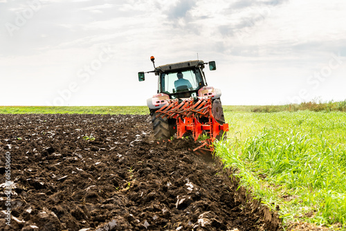 фотографія Tractor with plowing equipment preparing the soil in a green field under a clear