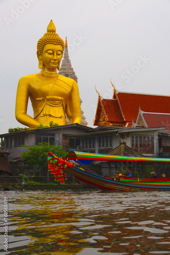 Big Golden Buddha.  Huge golden buddha towering above nearby buildings and river.  Boat in the foreground.