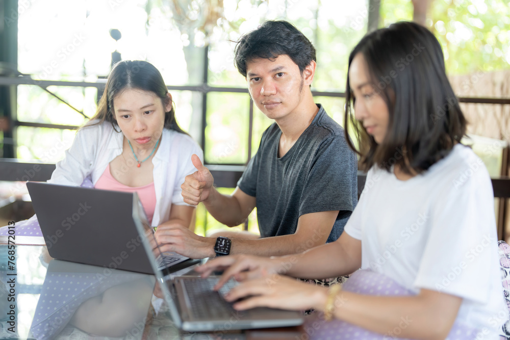 Asian male students give a thumbs up like symbol and three female classmates sit and type on a project on a laptop in a university faculty library, wearing casual clothes and giving confident glances. Asian male students give a thumbs up like symbol and three female classmates sit and type on a project on a laptop in a university faculty library, wearing casual clothes and giving confident glances.