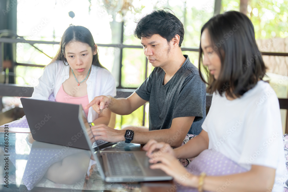 An Asian male student points his finger at a laptop screen with three female classmates in a university faculty library wearing casual clothes to study for a teacher's assignment. An Asian male student points his finger at a laptop screen with three female classmates in a university faculty library wearing casual clothes to study for a teacher's assignment.
