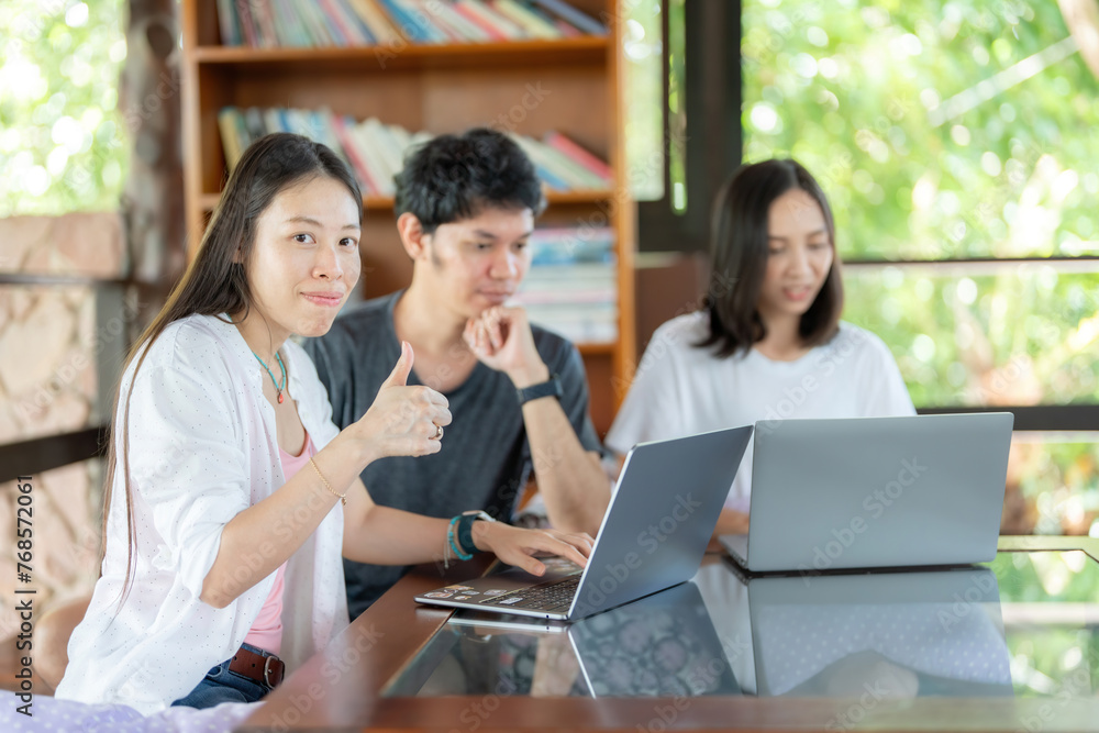 Side view of Asian female student with 2 friends studying online on laptop, thumbs up, like sign at university library, group reading books every week to gain knowledge and intelligence. Side view of Asian female student with 2 friends studying online on laptop, thumbs up, like sign at university library, group reading books every week to gain knowledge and intelligence.