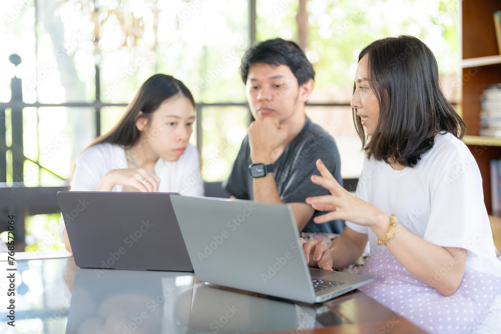 Group of Asian male and female students studying online in university faculty about subject with laptops in library Wear casual clothes and talk diligently with each other.