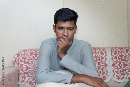 Indian man sadly sitting on the sofa at home