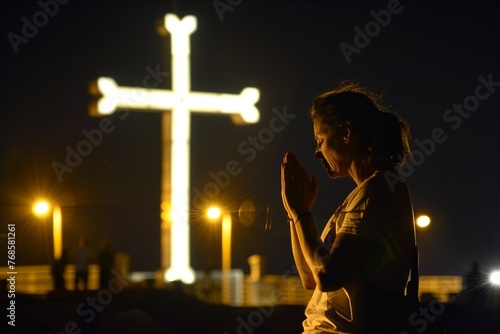 woman praying in front of illuminated cross at night