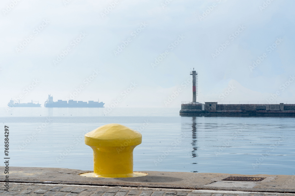 Golden beacon. Navigating Aegean sea's cargo ships Yellow maritime bitt. Concrete pier. Thessaloniki Greece 2024..