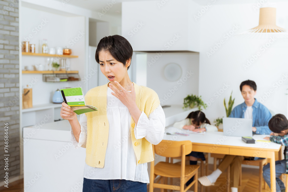 ダイニングルームで通帳を持つ主婦 ダイニングルームで通帳を持つ主婦