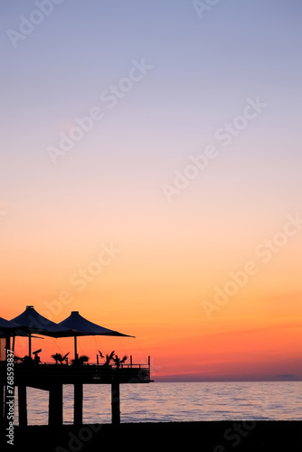 Tropical ocean beach with cafe on beach at dark sunset with purple orange sky. Vertical footage of water blue surface and dark coast. Travel, tourism, journey, destination on resort for relax concept.