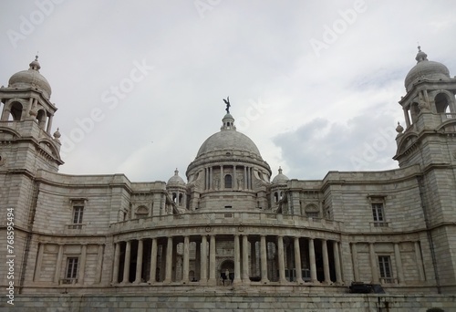 The grand Victoria Memorial Hall stands under a dramatic cloud-filled sky, showing off its exquisite colonial architecture with its towering domes and intricate stonework.