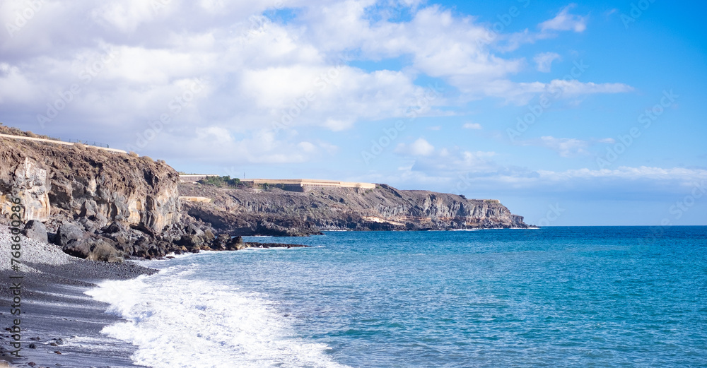 Tropical beach with black volcanic sand on south Tenerife travel tourism wide panorama background concept, blue sky, wallpaper
