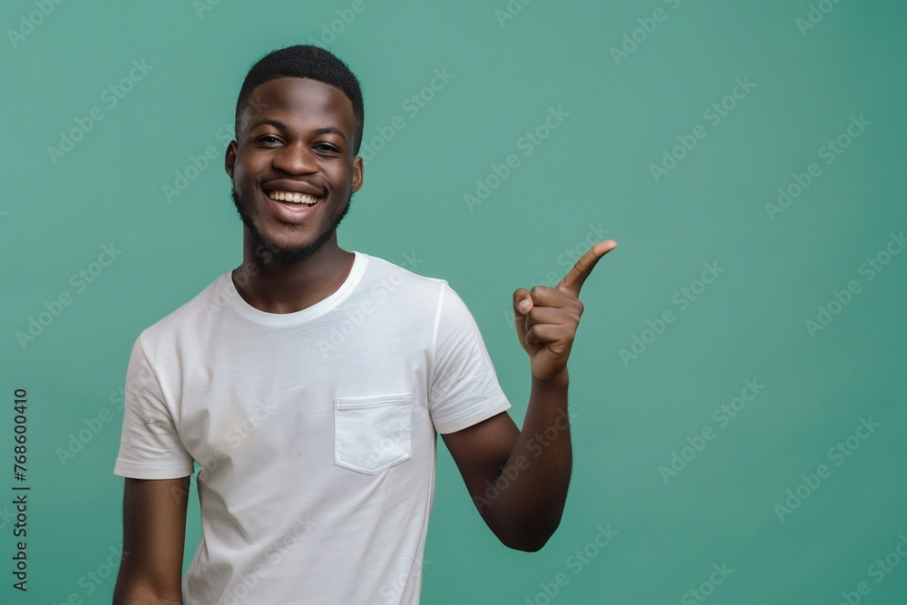 African american male person with toothy smile on face pointing with index finger on empty space over green background. Handsome young guy indicating place for advertising text in studio African american male person with toothy smile on face pointing with index finger on empty space over green background. Handsome young guy indicating place for advertising text in studio