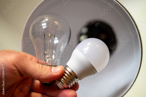 Men`s hand holding two light bulbs, one incandescent, the other LED, close up. Replacing old light bulb with new, energy-efficient LED, making home`s lightning better