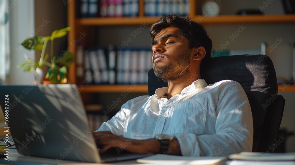 Relaxed Young Indian Man Rests with Closed Eyes Amidst Office Work Relaxed Young Indian Man Rests with Closed Eyes Amidst Office Work