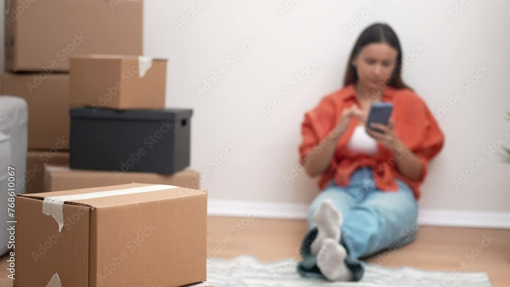 A young, joyful woman embraces moving day in her new home, surrounded by carton boxes, happily engaged in a video call with friends A young, joyful woman embraces moving day in her new home, surrounded by carton boxes, happily engaged in a video call with friends