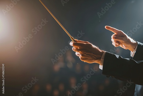 Closeup of an orchestra conductor's hands holding the baton and pointing towards his students. Musical performance at concert hall, blurred background. Copy space. Theater. Maestro. Director. Leader photo