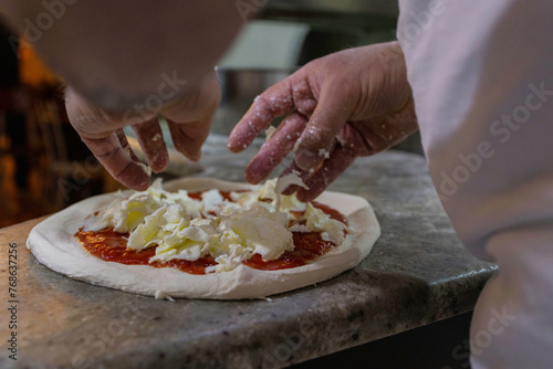 Pizzaiolo napoletano mentre adagia della mozzarella di bufala su una pizza tradizionale napoletana 