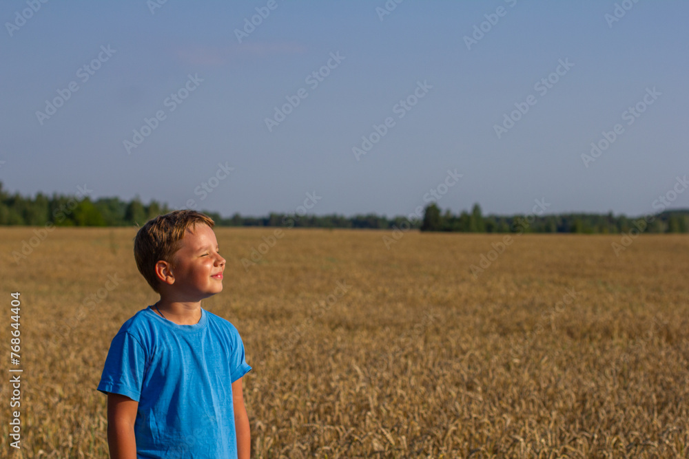 A beautiful child smiles while standing in a wheat field under the rays of the summer sun Copy space. Place for an inscription. A child enjoys the warmth of the summer sun in a wheat field in summer. A beautiful child smiles while standing in a wheat field under the rays of the summer sun Copy space. Place for an inscription. A child enjoys the warmth of the summer sun in a wheat field in summer.