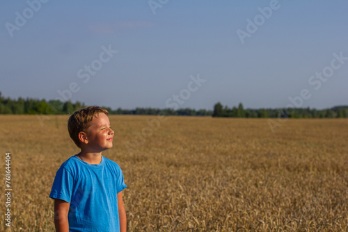 A beautiful child smiles while standing in a wheat field under the rays of the summer sun Copy space. Place for an inscription. A child enjoys the warmth of the summer sun in a wheat field in summer.