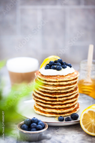 Stack of freshly prepared lemon poppy seed pancakes topped with sour cream and blueberries