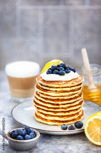 Stack of freshly prepared lemon poppy seed pancakes topped with sour cream and blueberries