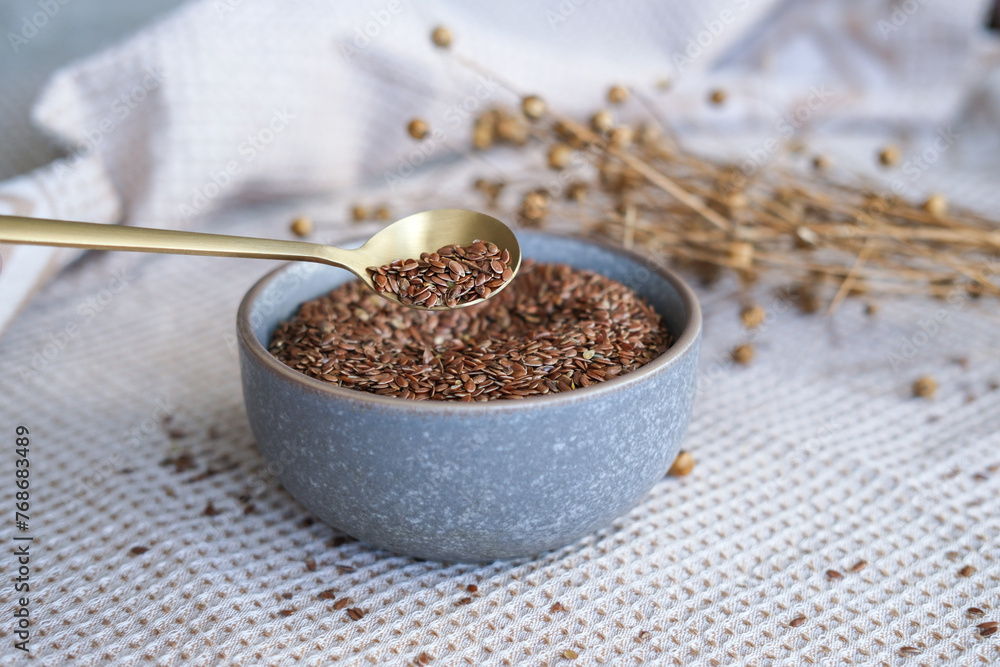 Golden teaspoon of flax seeds in a bowl and dried flax flowers on a cotton napkin background. Organic food, veganism, vitamins, health. Selective focus Golden teaspoon of flax seeds in a bowl and dried flax flowers on a cotton napkin background. Organic food, veganism, vitamins, health. Selective focus