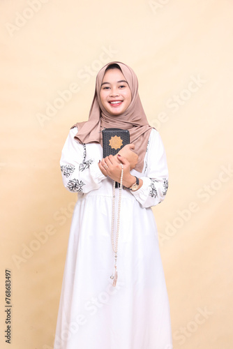 beautiful mature Asian Muslim woman in hijab smiling cheerfully hugging quran and holding prayer beads. for advertising, lifestyle, banners and Ramadan