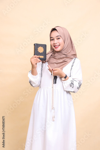 beautiful indonesia Muslim adult woman in hijab cheerful expression looking at camera holding prayer beads and carrying quran by offering it. for advertising, lifestyle, banners and Ramadan