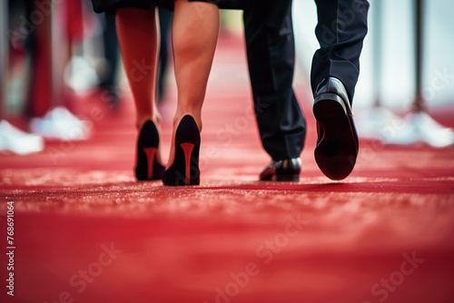 A couple in luxurious business attire walks the red carpet, close up view of the carpet and legs 