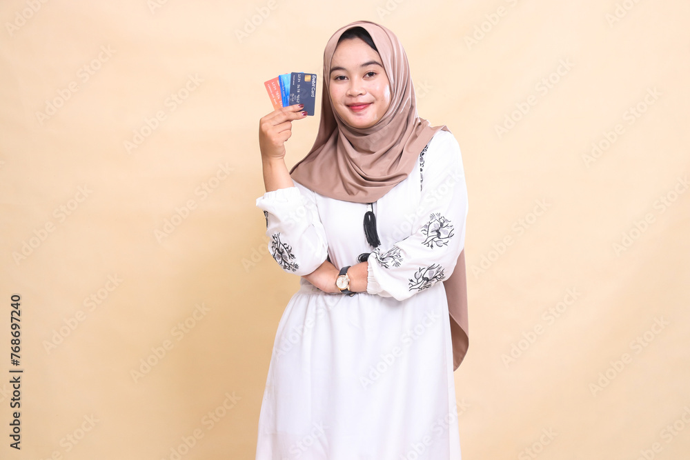 a beautiful Asian Muslim woman wearing a hijab with a graceful smile with her arms crossed carrying a debit credit card to her side for payment. used for advertising, technology, Eid and Ramadan a beautiful Asian Muslim woman wearing a hijab with a graceful smile with her arms crossed carrying a debit credit card to her side for payment. used for advertising, technology, Eid and Ramadan