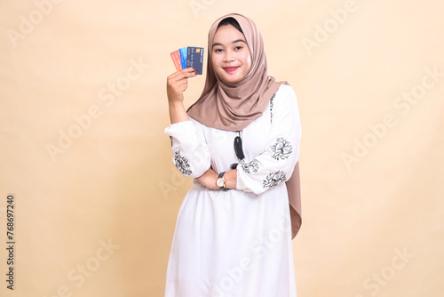 a beautiful Asian Muslim woman wearing a hijab with a graceful smile with her arms crossed carrying a debit credit card to her side for payment. used for advertising, technology, Eid and Ramadan