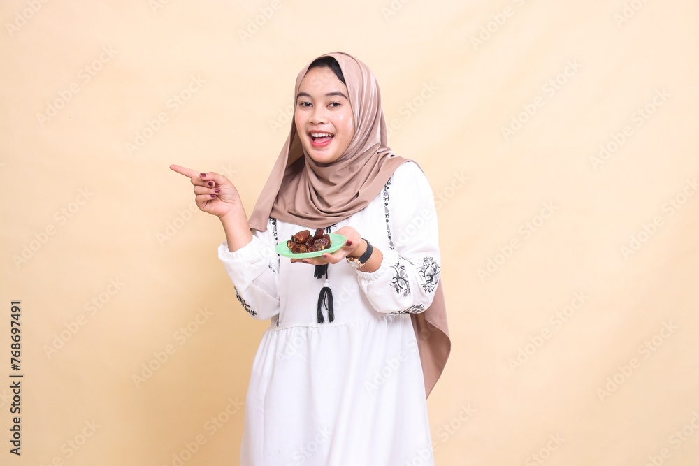 a beautiful indonesia Muslim girl wearing a hijab likes to point to the right and bring dates for the sahur menu and breaking the fast. used for advertising, health, Eid and Ramadan